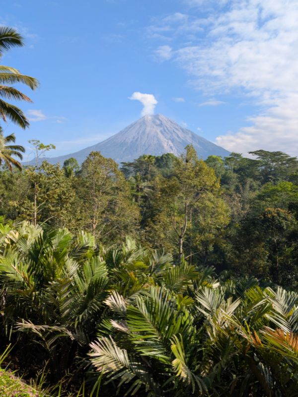 Mount Semeru erupting in the distance behind the Tumpak Sewu waterfall area in East Java